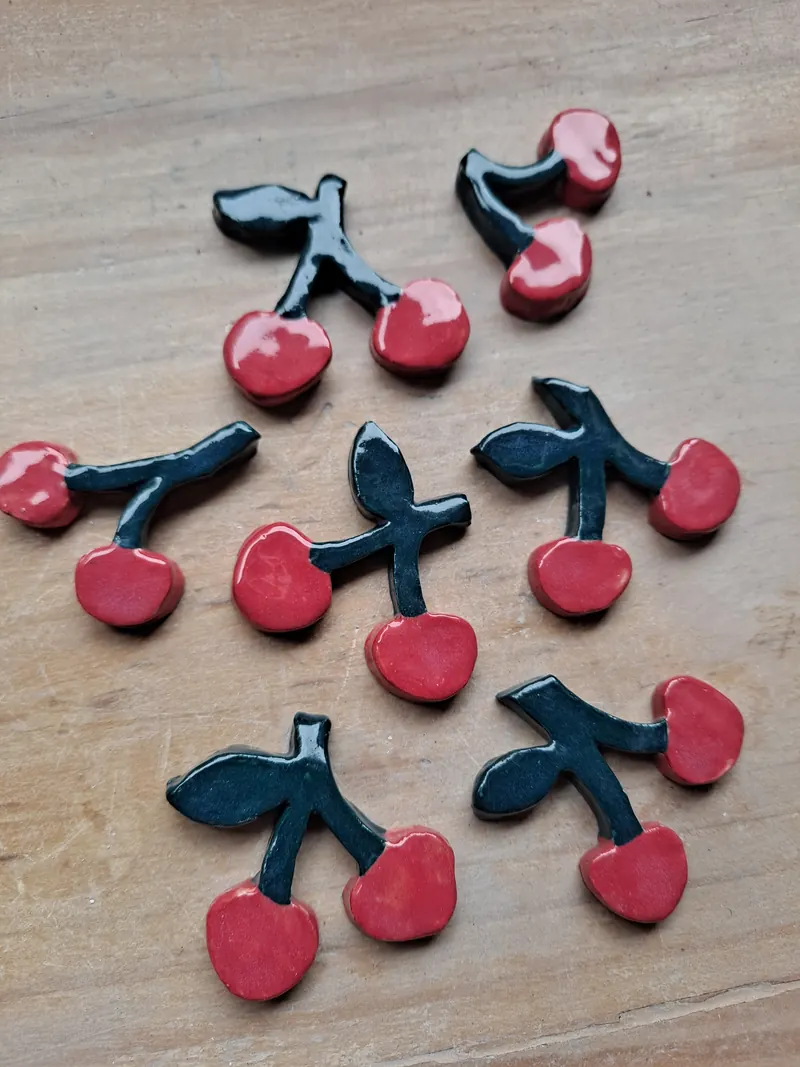 Cerezas de cerámica esmaltadas en rojo y negro sobre una mesa de madera