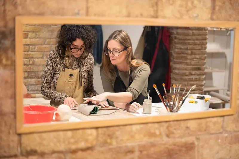 Dos alumnas trabajando el barro en el taller, vistas a través de un espejo
