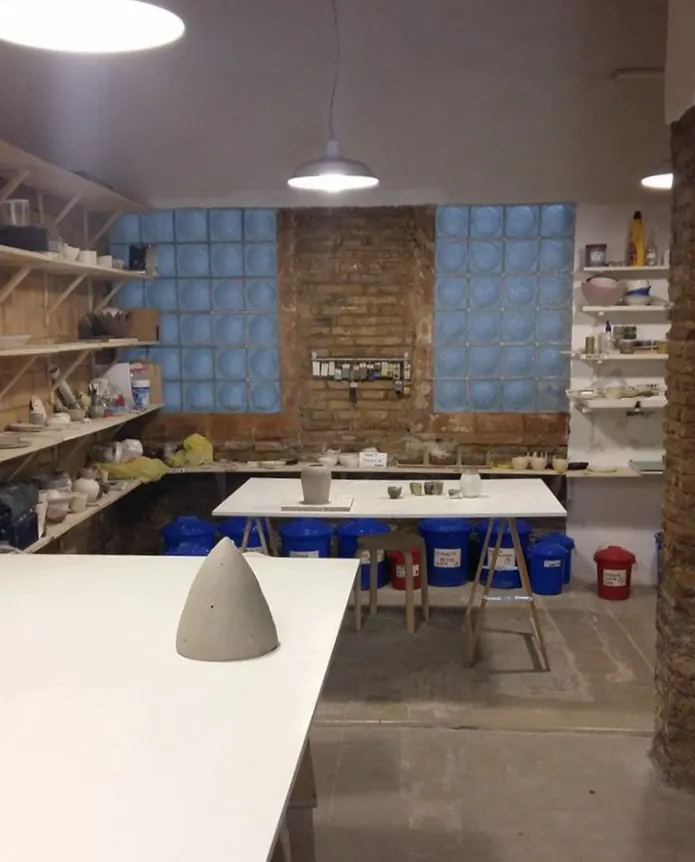 Interior del taller de LittleStudio Ceramics con la mesa grande, estanterías de piezas y ventanas de pavés
