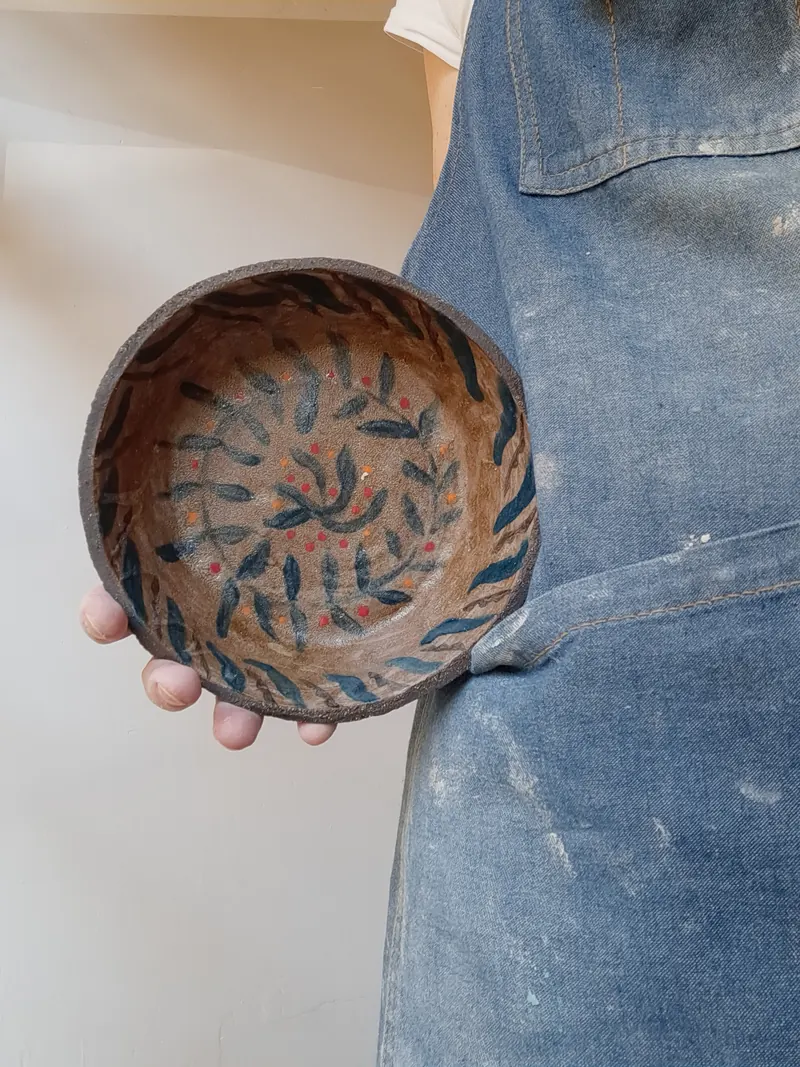 Cuenco de cerámica pintado a mano con hojas, sobre un delantal vaquero
